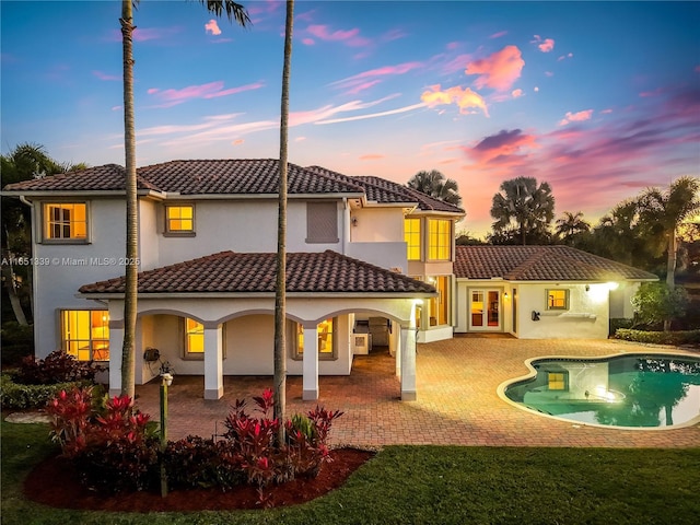 14403 S Jockey Cir S, Davie, FL 33330 - back of house at dusk with stucco siding, a tiled roof, an outdoor pool, a patio area, and a yard