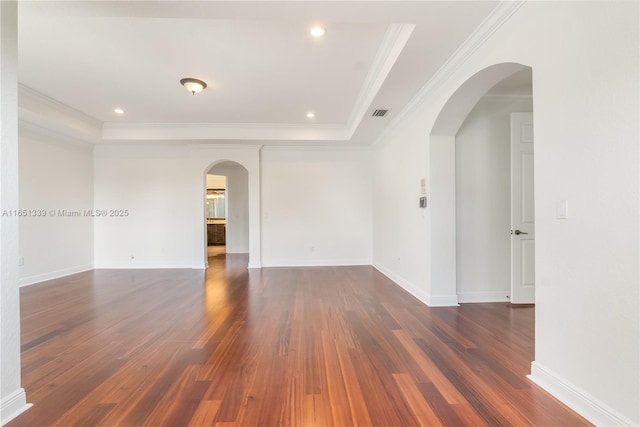 spare room with arched walkways, a tray ceiling, dark wood-type flooring, and crown molding