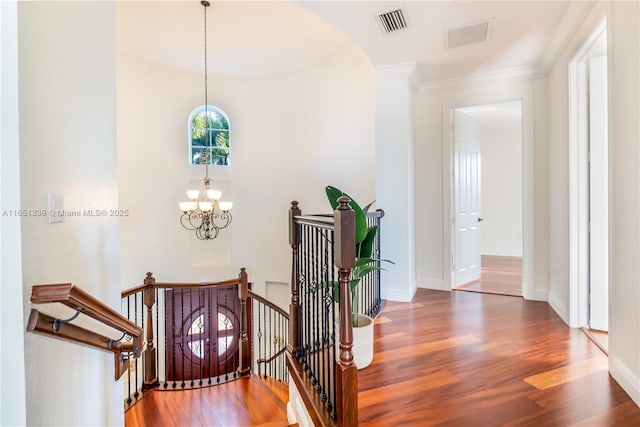 corridor with a notable chandelier, visible vents, baseboards, an upstairs landing, and dark wood-style floors