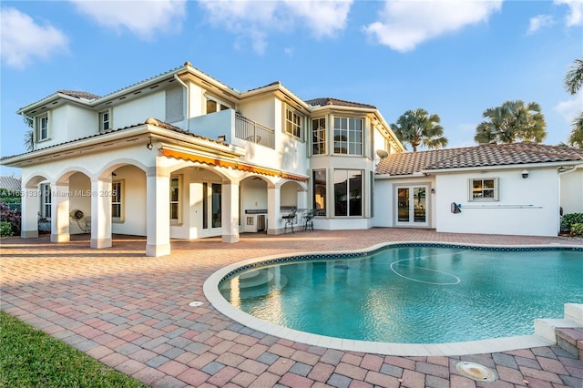 rear view of house featuring french doors, a patio, stucco siding, a balcony, and an outdoor pool