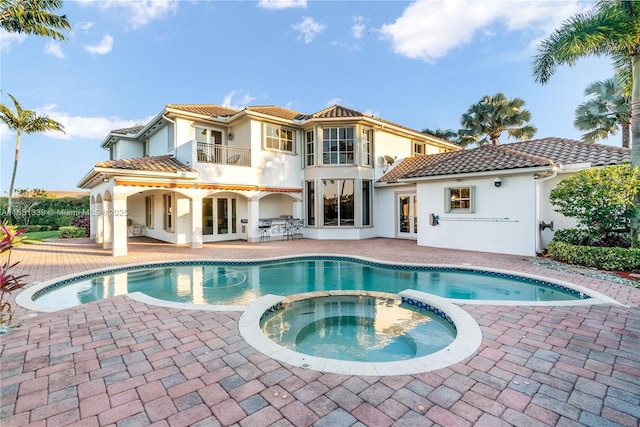 back of house featuring a balcony, a tiled roof, a patio area, a pool with connected hot tub, and stucco siding