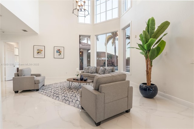 living room with a notable chandelier, marble finish floor, a towering ceiling, and baseboards