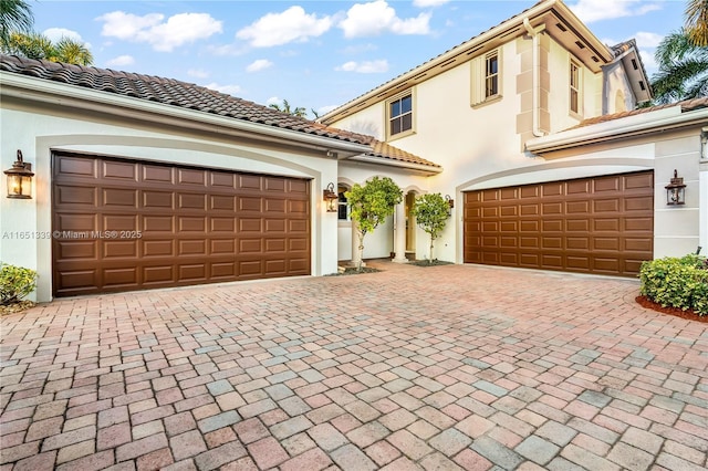 mediterranean / spanish house featuring a tiled roof, decorative driveway, and stucco siding