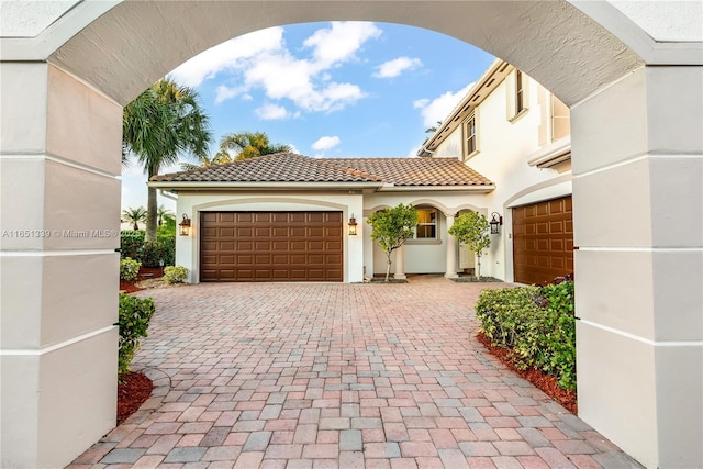 view of front of home with a garage, a tile roof, decorative driveway, and stucco siding