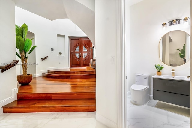 interior space featuring marble finish floor, baseboards, vanity, and toilet