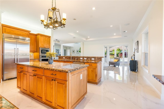 kitchen with built in appliances, a kitchen island, open floor plan, light stone countertops, and a tray ceiling