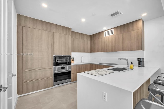 kitchen featuring oven, sink, built in microwave, light tile patterned flooring, and kitchen peninsula