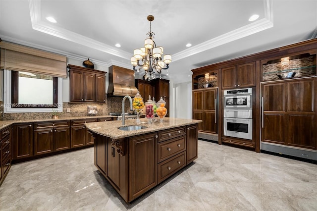 kitchen featuring a center island with sink, hanging light fixtures, a raised ceiling, and dark brown cabinetry