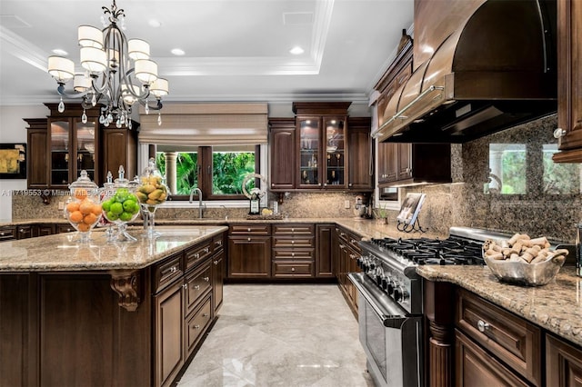 kitchen with custom exhaust hood, stainless steel stove, a raised ceiling, a chandelier, and dark brown cabinets