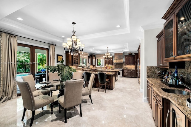 dining room with sink, a wealth of natural light, a tray ceiling, and a notable chandelier