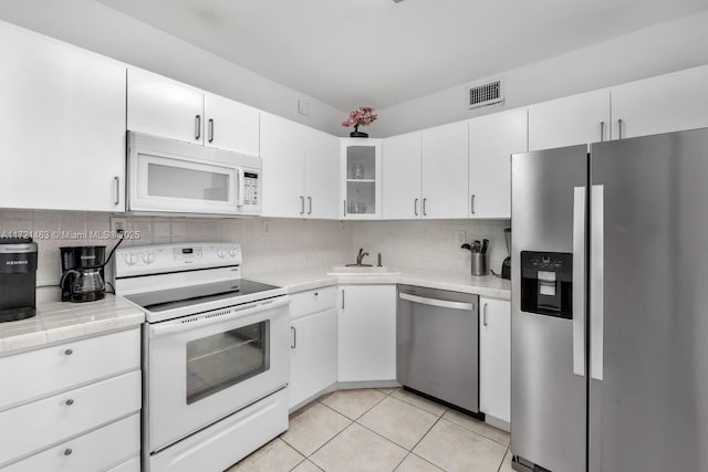 kitchen featuring appliances with stainless steel finishes, backsplash, sink, light tile patterned floors, and white cabinetry