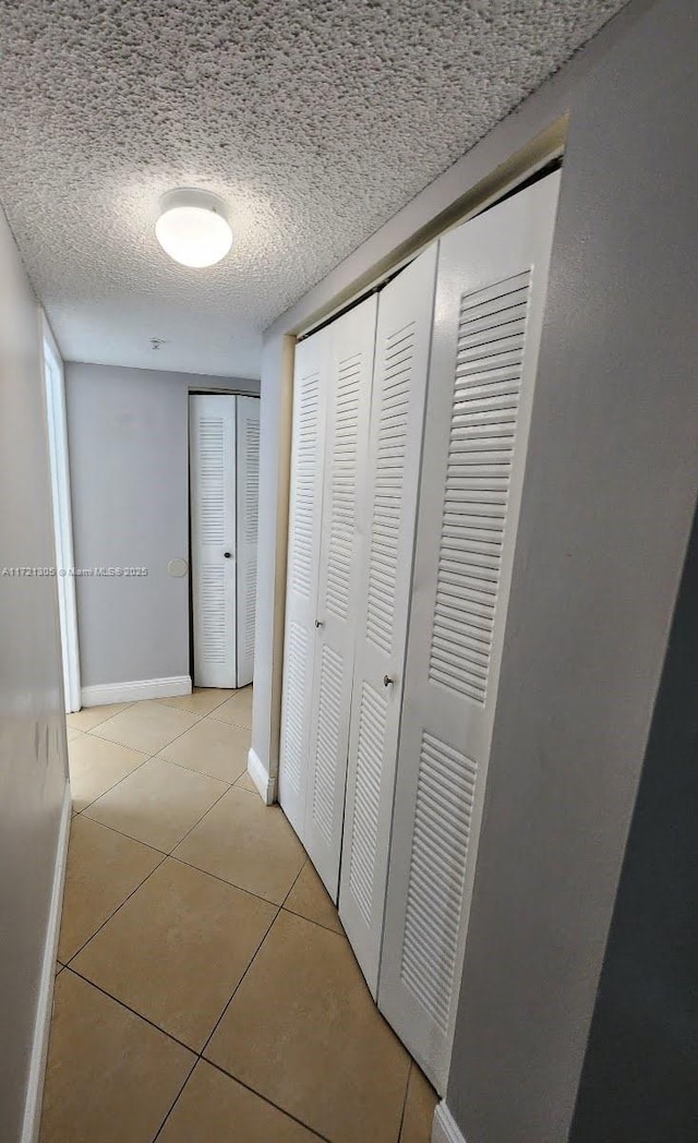 hall with a textured ceiling and light tile patterned floors