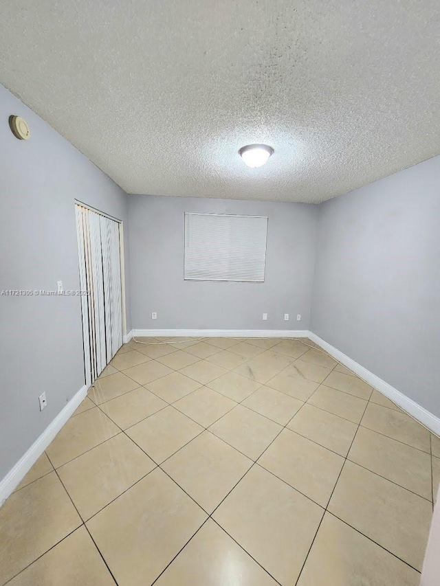 empty room with a textured ceiling and light tile patterned flooring