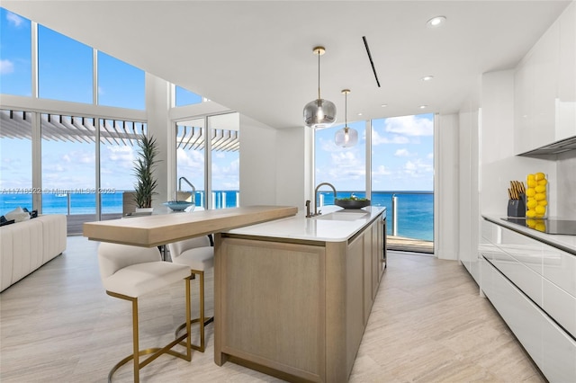 kitchen featuring white cabinets, a kitchen island with sink, a water view, and hanging light fixtures