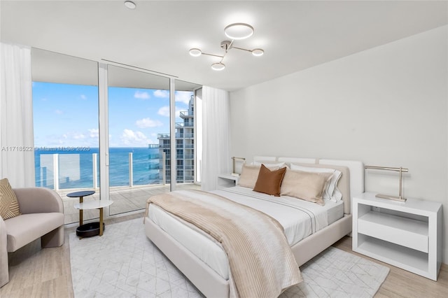 bedroom with floor to ceiling windows, a water view, and light hardwood / wood-style flooring