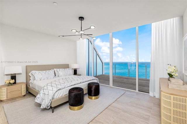 bedroom featuring access to outside, a water view, light hardwood / wood-style flooring, and a wall of windows