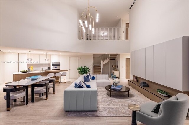 living room with a towering ceiling, a chandelier, and light wood-type flooring