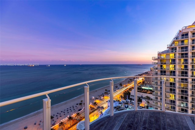 balcony at dusk featuring a water view and a view of the beach