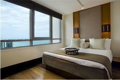 bedroom featuring light hardwood / wood-style floors, a water view, and rail lighting