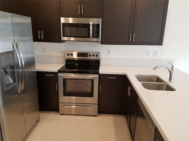 kitchen with appliances with stainless steel finishes, dark brown cabinetry, light tile patterned floors, and sink