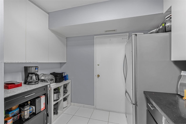 kitchen with white cabinets, light tile patterned floors, stainless steel fridge, and dark stone countertops