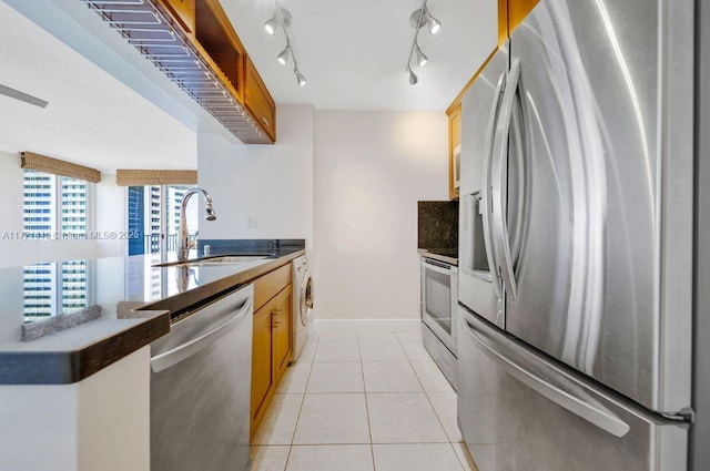 kitchen featuring sink, backsplash, washer / dryer, light tile patterned floors, and appliances with stainless steel finishes