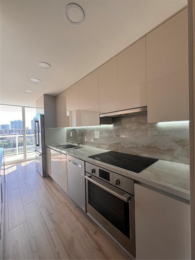 kitchen featuring floor to ceiling windows, backsplash, sink, light wood-type flooring, and stainless steel appliances