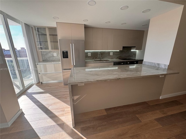 kitchen featuring kitchen peninsula, stainless steel fridge with ice dispenser, light stone counters, and sink