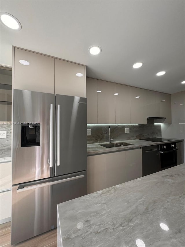 kitchen with gray cabinetry, sink, light hardwood / wood-style flooring, dark stone counters, and black appliances