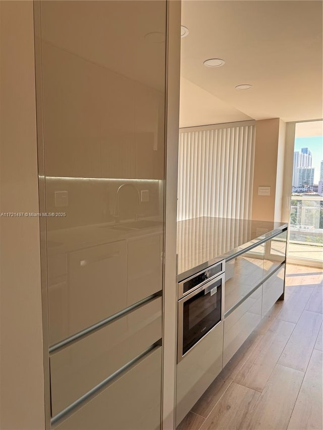 kitchen with stainless steel oven, light wood-type flooring, and floor to ceiling windows