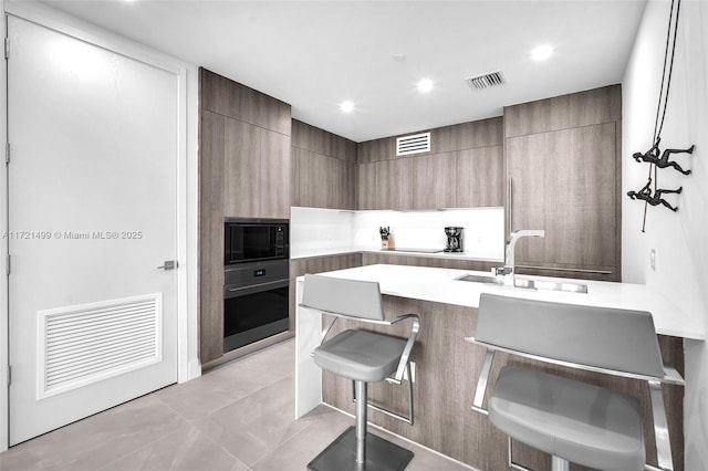 kitchen with kitchen peninsula, stainless steel oven, black microwave, sink, and a breakfast bar area