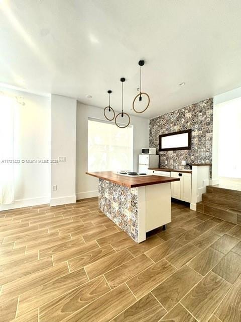 kitchen featuring white cabinets, wood counters, a center island, and hanging light fixtures