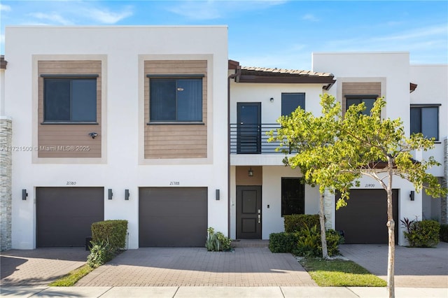 townhome / multi-family property with decorative driveway, a tile roof, a balcony, and stucco siding