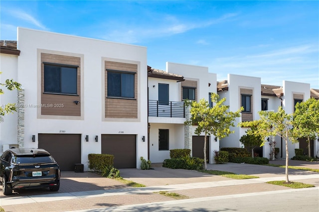 view of front facade with a balcony, driveway, an attached garage, and stucco siding