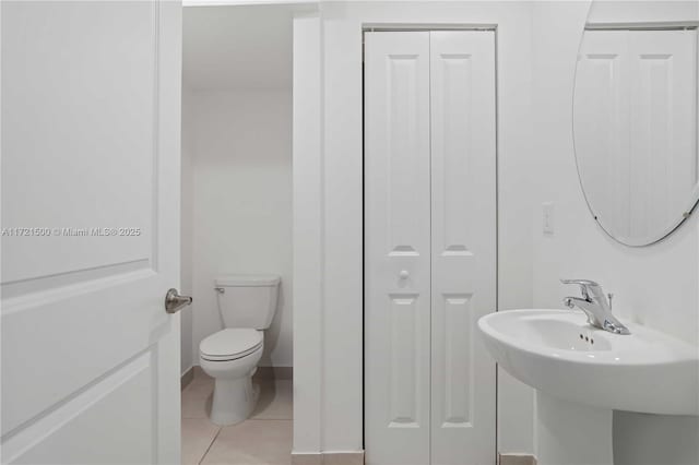 bathroom with a closet, toilet, a sink, tile patterned flooring, and baseboards