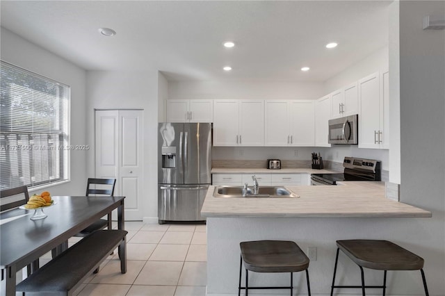 kitchen featuring stainless steel appliances, a peninsula, a sink, light countertops, and a kitchen bar