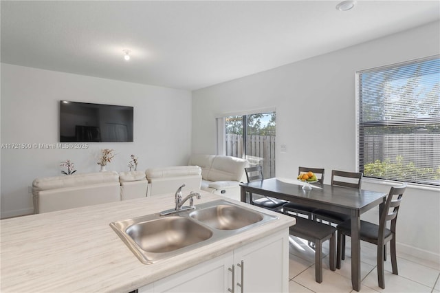 kitchen featuring light tile patterned floors, light countertops, open floor plan, white cabinetry, and a sink