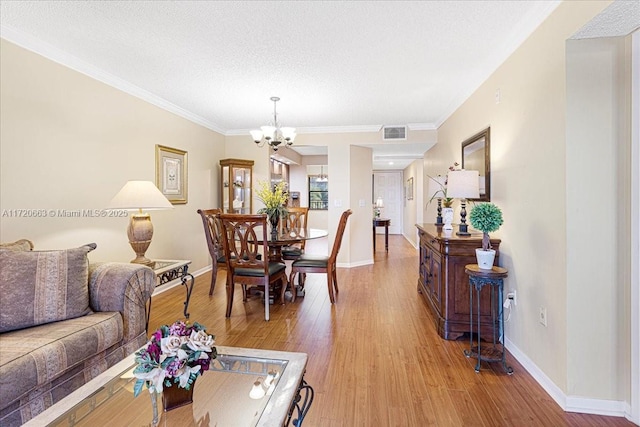 interior space with a textured ceiling, light wood-type flooring, ornamental molding, and an inviting chandelier