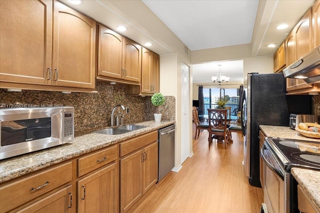 kitchen with light stone countertops, sink, an inviting chandelier, decorative backsplash, and appliances with stainless steel finishes