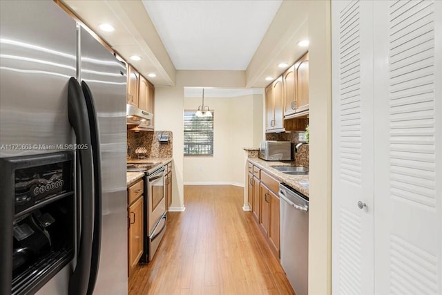 kitchen with appliances with stainless steel finishes, backsplash, decorative light fixtures, and light stone counters