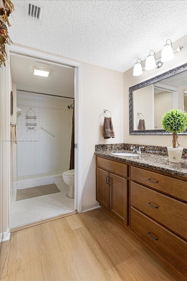 bathroom with a shower with shower curtain, a textured ceiling, vanity, wood-type flooring, and toilet