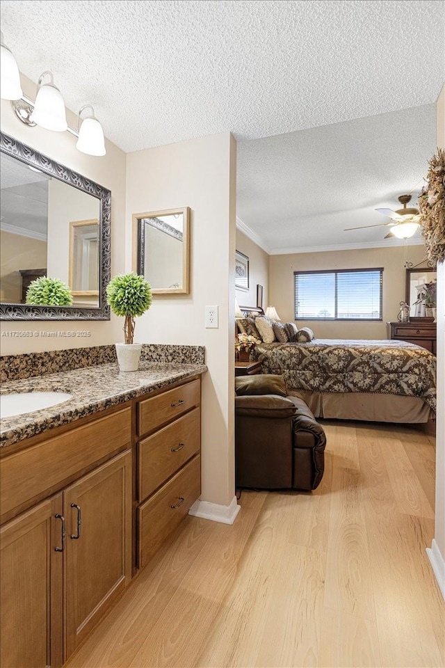 bathroom with hardwood / wood-style floors, vanity, ceiling fan, ornamental molding, and a textured ceiling