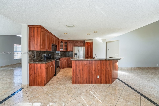 kitchen with tasteful backsplash, light tile patterned floors, dark stone counters, a center island with sink, and appliances with stainless steel finishes