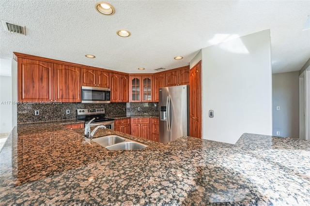 kitchen featuring sink, dark stone countertops, kitchen peninsula, backsplash, and appliances with stainless steel finishes