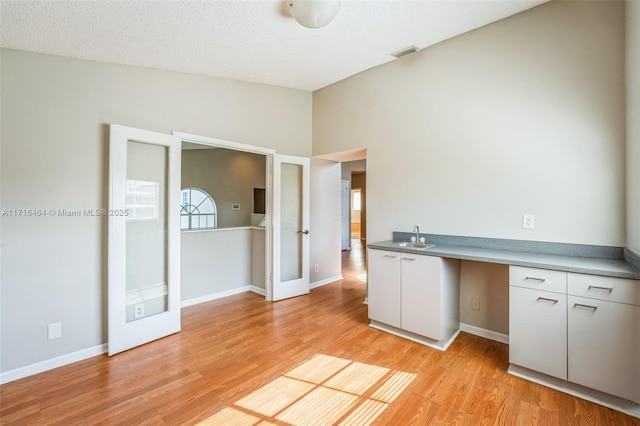 kitchen featuring sink, built in desk, white cabinetry, a textured ceiling, and french doors