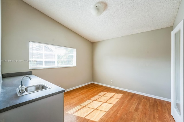 interior space with vaulted ceiling, a textured ceiling, light wood-type flooring, and sink