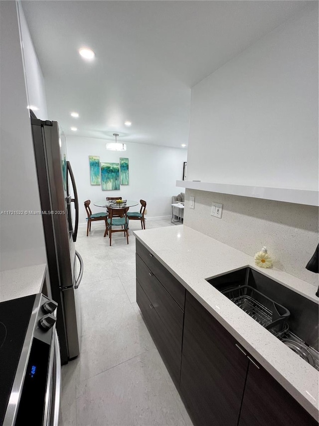 kitchen featuring stainless steel refrigerator, dark brown cabinetry, sink, backsplash, and range