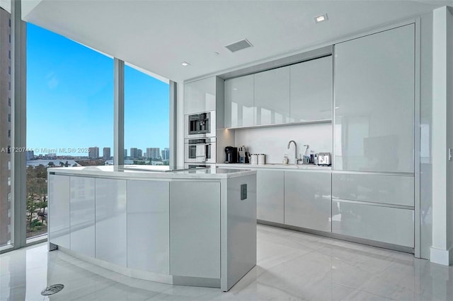 kitchen with a kitchen island, double oven, sink, a wall of windows, and white cabinetry