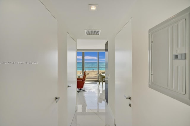 corridor featuring a beach view, electric panel, a water view, and a wall of windows