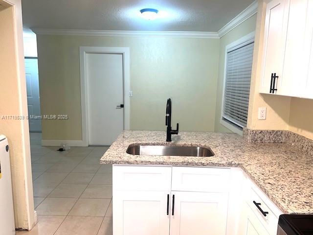 1574 NW 7th Ln, Pompano Beach, FL 33060 - kitchen featuring white cabinets, a peninsula, light stone countertops, light tile patterned flooring, and ornamental molding